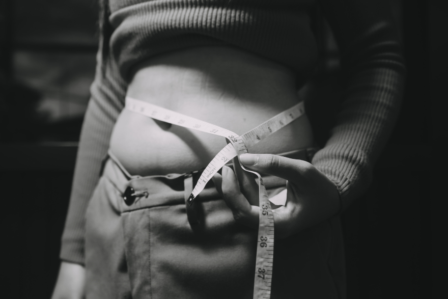 Tirzepatide before-and-after: a woman measuring herself, black-and-white photo.